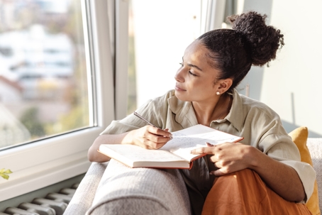 woman looking out the window while journaling
